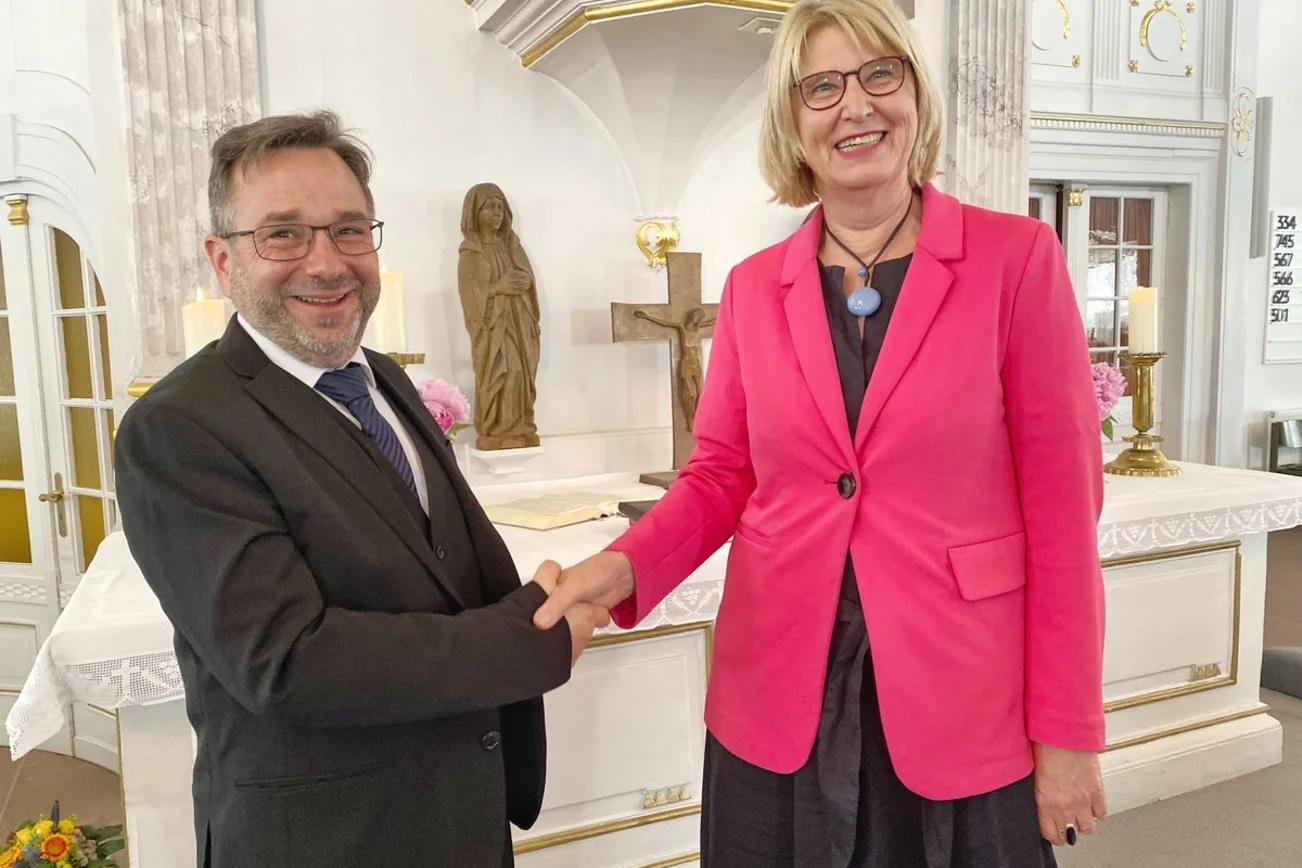 Zwei Personen reichen sich in einer Kirche die Hände.