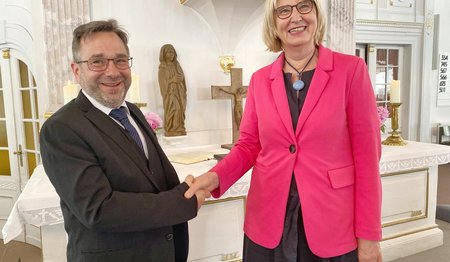 Zwei Personen reichen sich in einer Kirche die Hände.