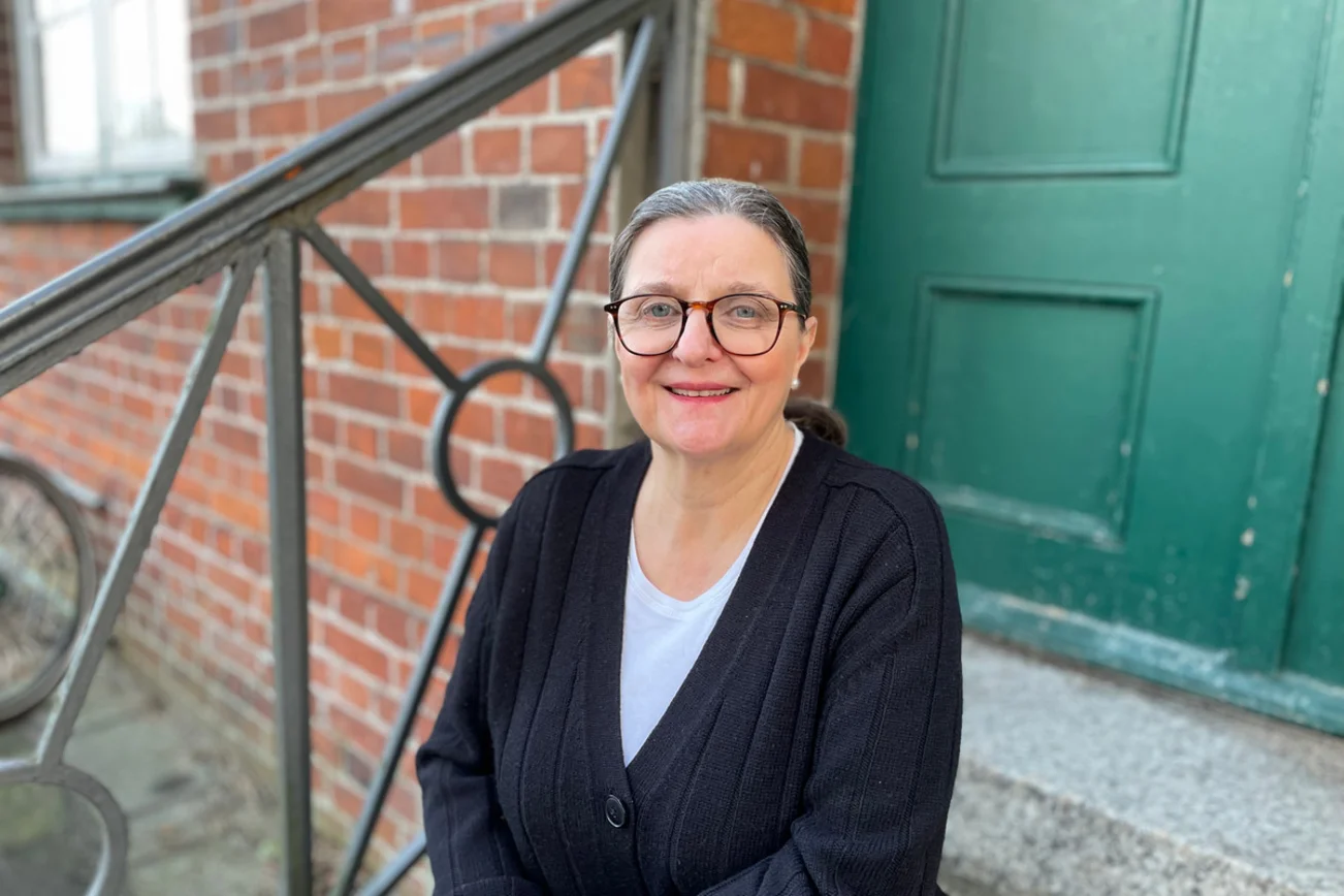 Eine Frau sitzt vor einer Tür und schaut freundlich in die Kamera.