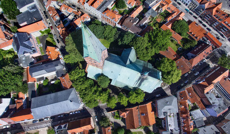 Aus der Vogelperspektive ist die St. Aegiedien-Kirche zu sehen, grüne Bäume umsäumen die Kirche - Rund um die Kirche sind die Straßen und Dächer Lübecks zu sehen.