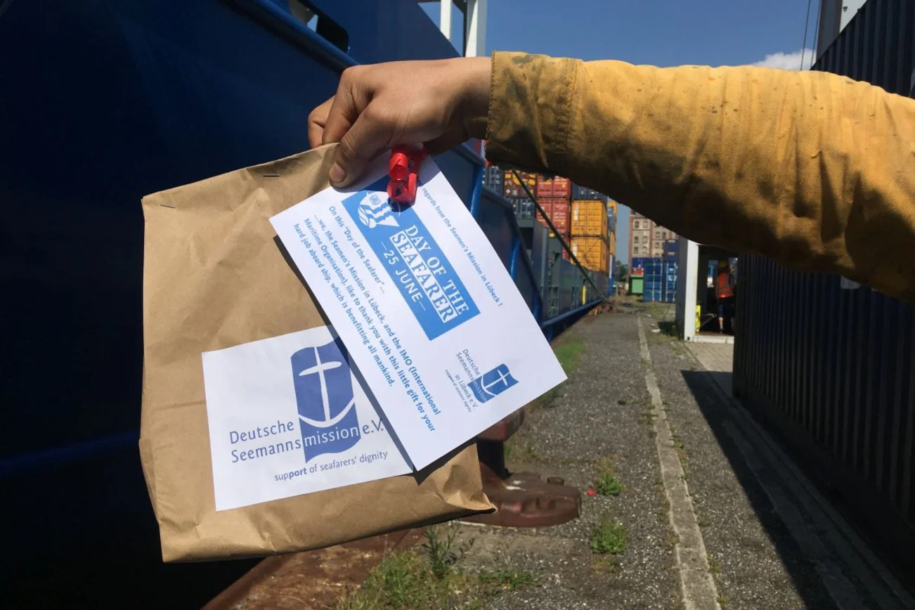 Die Hand eines Seefahrers hält ein Päckchen der Deutschen Seemannsmission in der Hand. 
