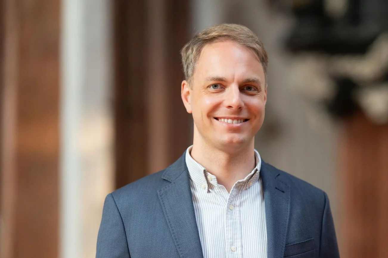 Ein Man mit blauem Sacko und kurzen blonden Haaren lächelt in die Kamera.