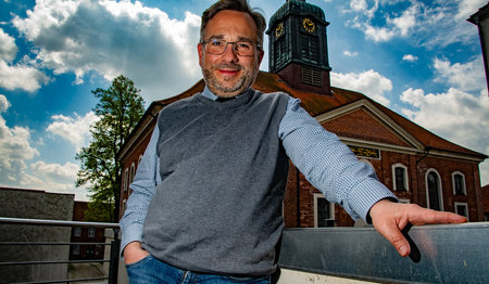 Ein mann steht vor einer Kirche und lächelt in die Kamera. 