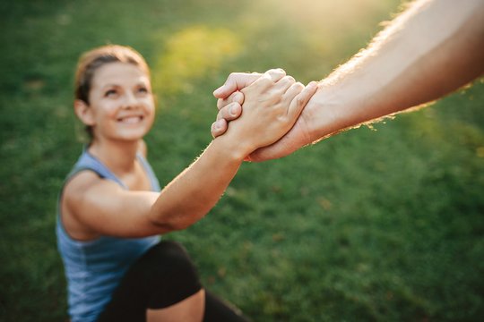 Eine Frau sitzt auf dem Rasen und hält die Hand einer Person von der nicht mehr zu sehen ist. Es scheint die Sonne, die man aber nicht sieht. Die Frau lächelt.