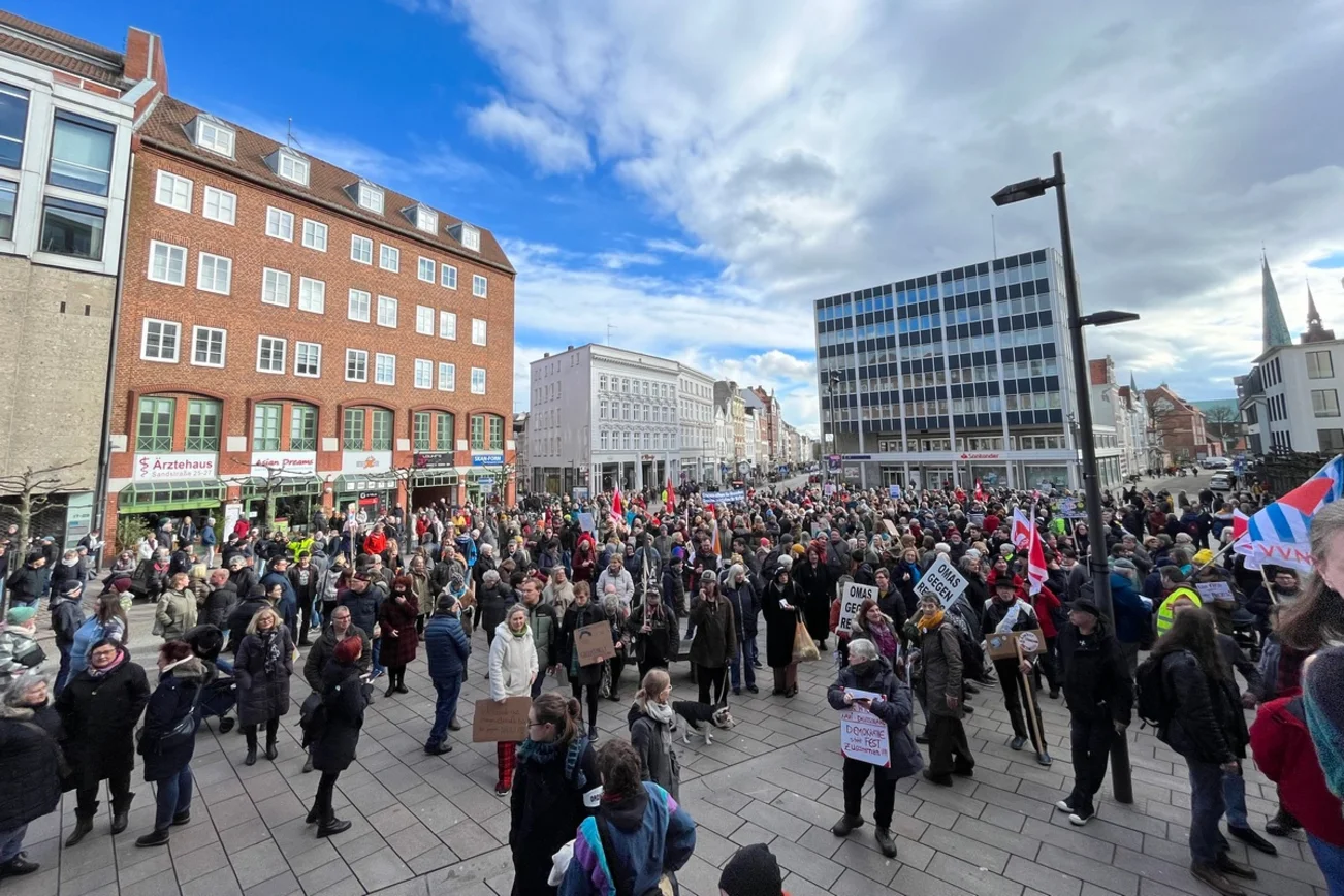Viele Menschen mit gebastelten Schildern stehen zusammen.