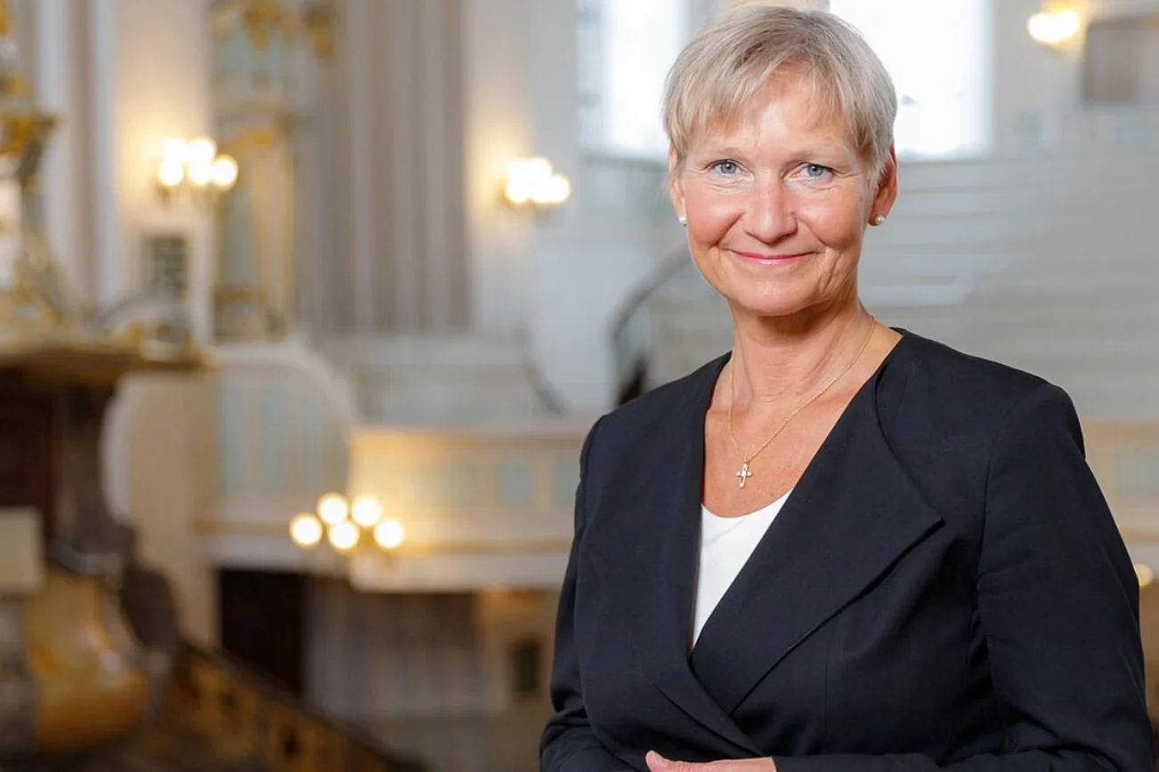 Eine Frau blickt freundliche lächelnd in die Kamera. Im Hintergrund unscharf ein Kirchenraum.