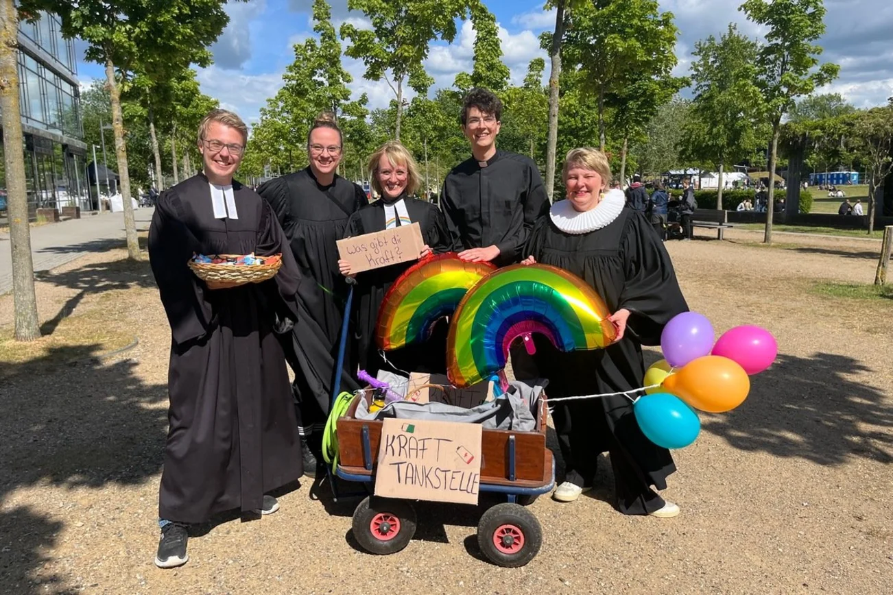 Fünf Menschen in Talar hinter einem gefüllten Bollerwagen.