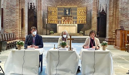 Drei Personen an einem Tisch in einer Kirche