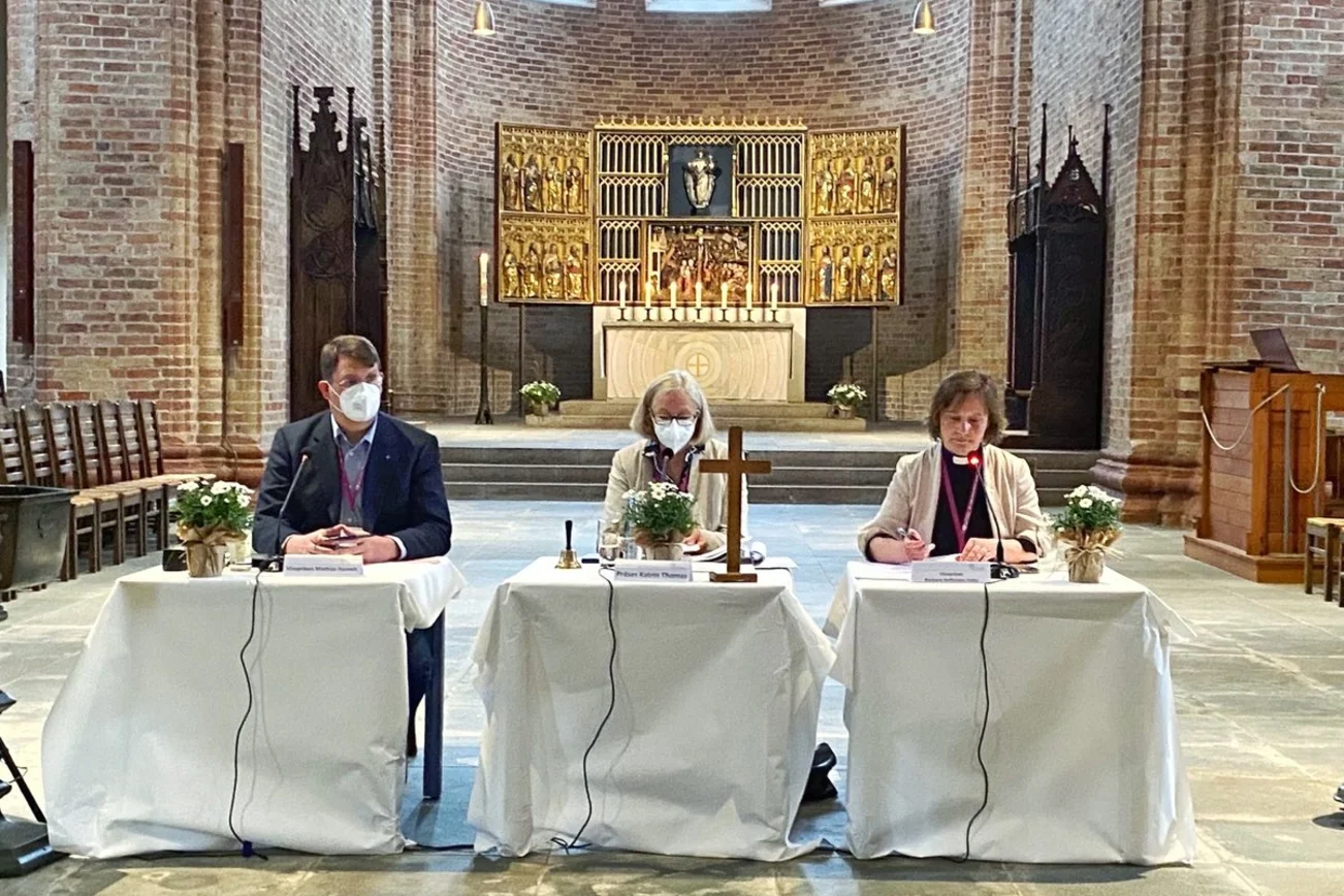Drei Personen an einem Tisch in einer Kirche