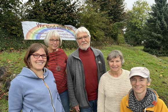 Vier Frauen und ein Mann stehen vor einem Banner mit dem Schriftzug "Wir sind nicht still"