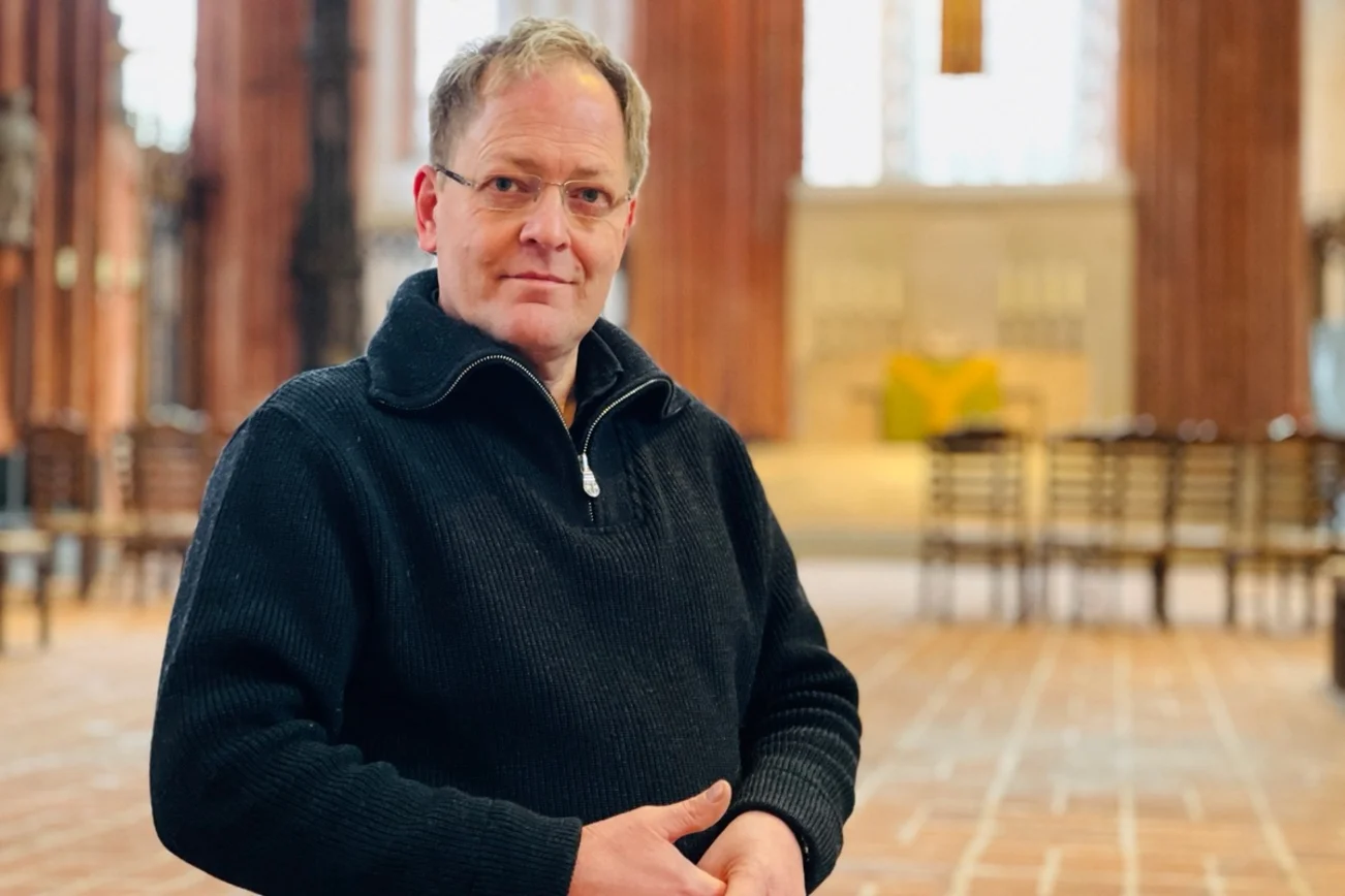 Mann mit Brille steht in der Marienkirche und schaut nachdenklich in die Kamera