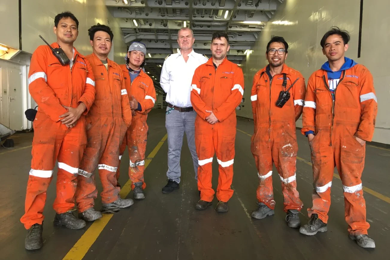 Eine Gruppe von Männern steht in einem Schiff und blickt in die Kamera. 