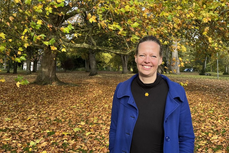 Junge Frau steht vor einem Baum und schaut lächelnd in die Kamera, viel Herbstlaub liegt um sie herum. - Copyright: Katharina Micheel