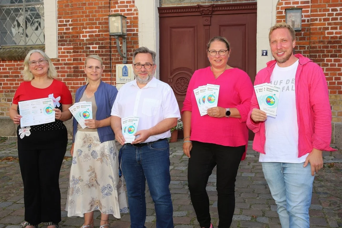 Fünf Personen stehen nebeneinander und halten Flyer und gucken zum Betrachter.