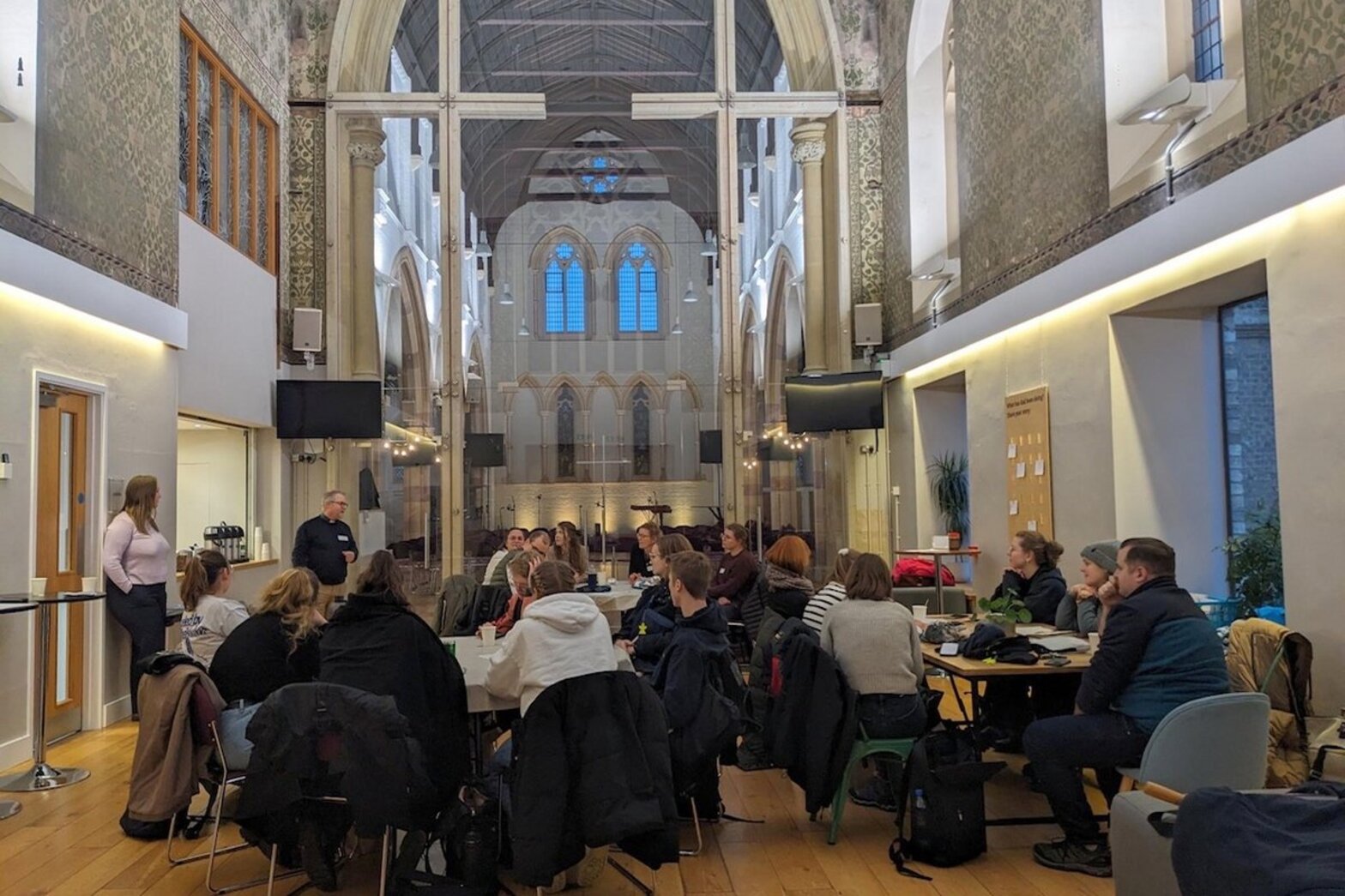 Blick in einen Saal mit hohen Decken und Menschen an Tischen