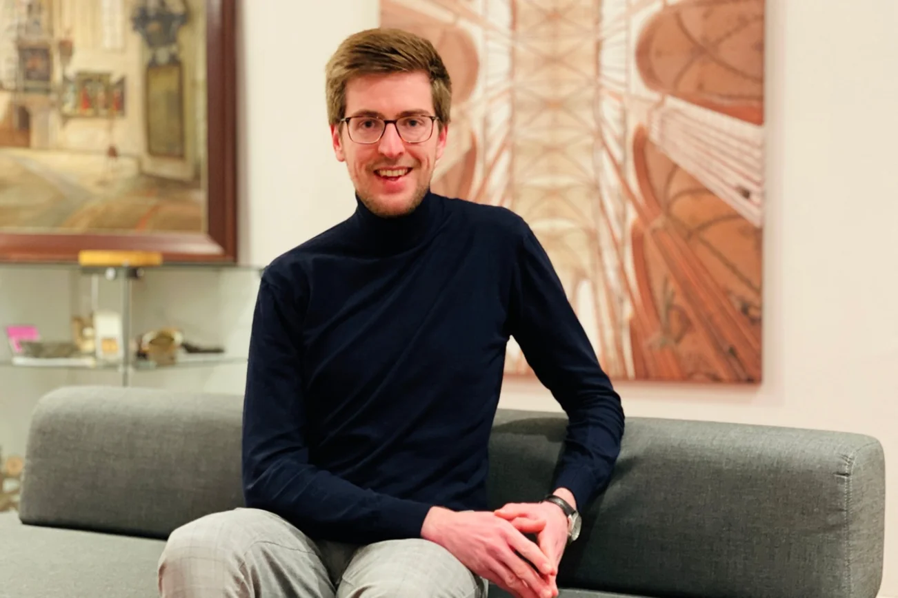 Junger Mann sitzt auf einer Couch und lächelt in die Kamera.