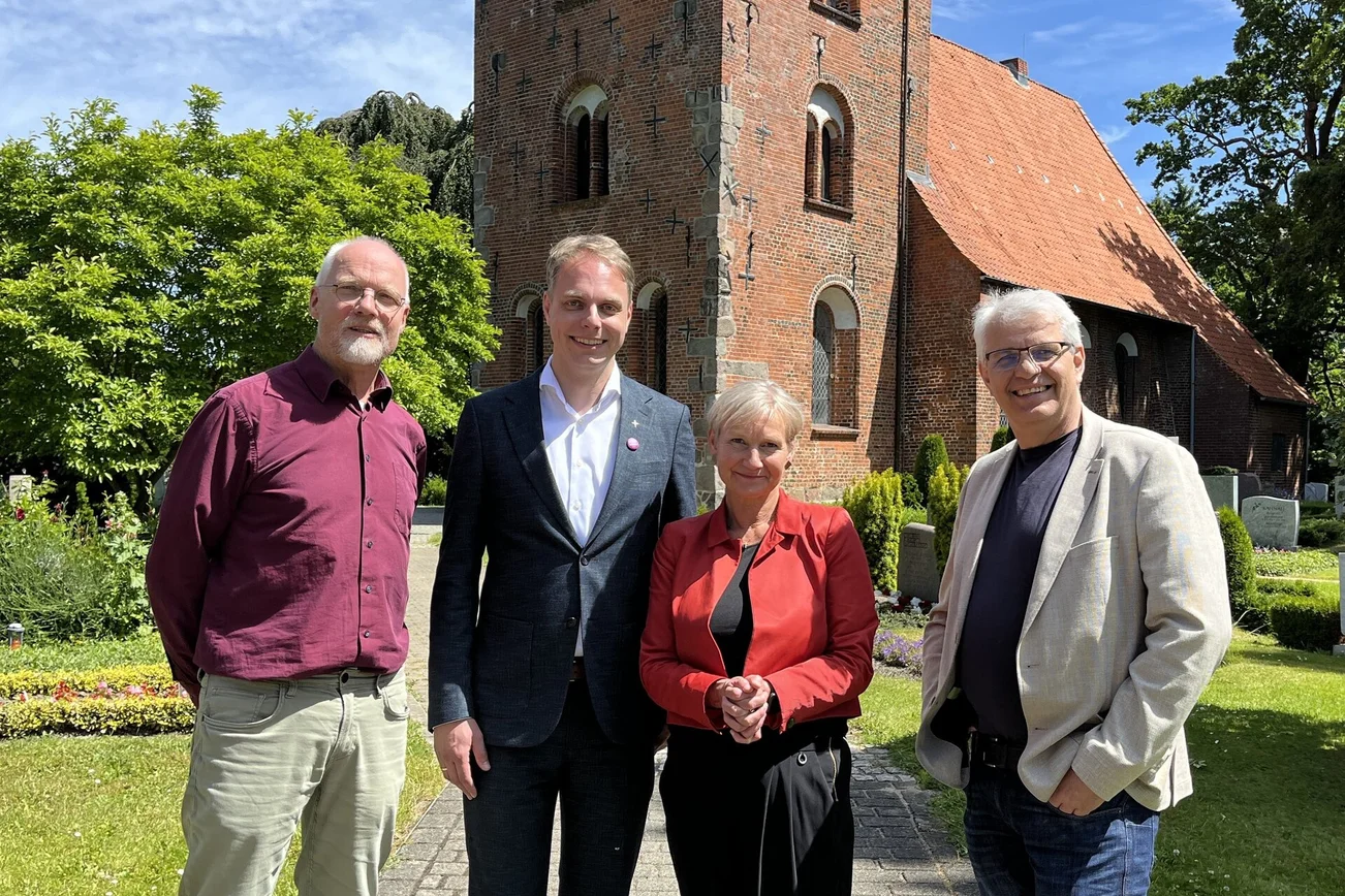 Drei Männer und eine Frau stehen vor eine Kirche.