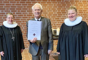 Drei Personen stehen in einer Kirche und lächeln in die Kamera. In der Mitte steht ein Mann mit einer Urkunde. - Copyright: Bastian Modrow