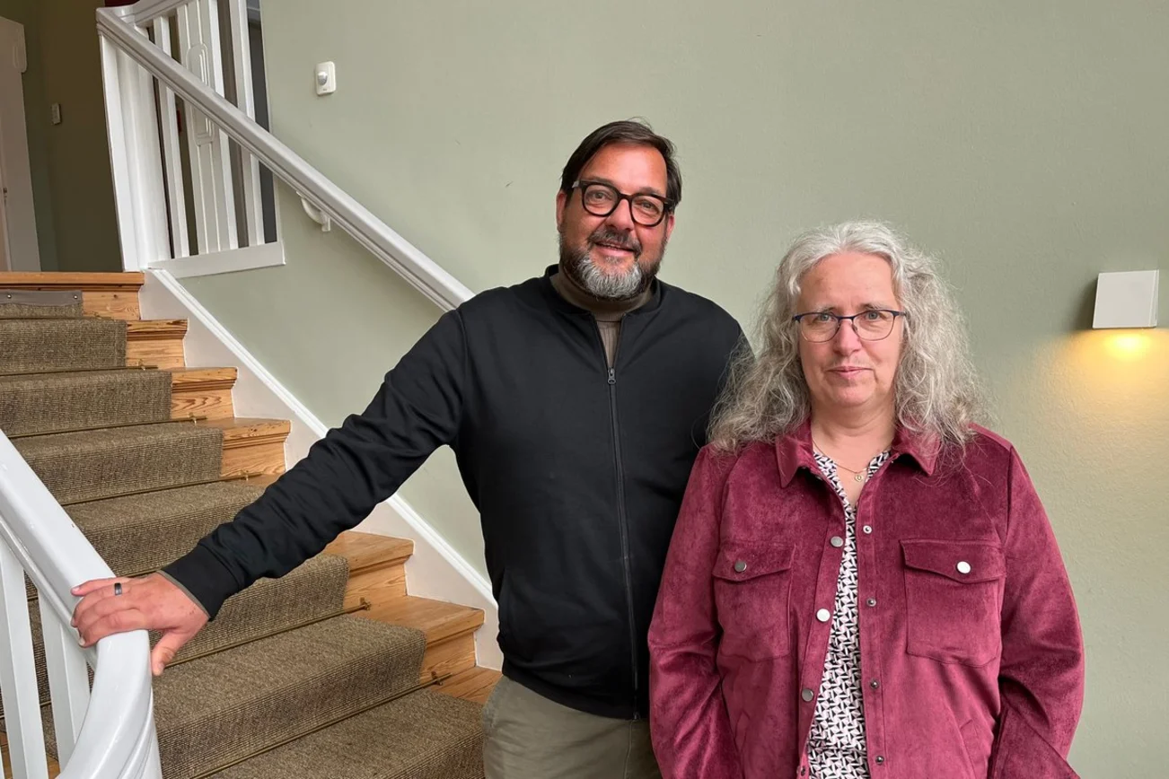 Ein Mann und eine Frau stehen in einem Treppenhaus und lächeln in die Kamera.