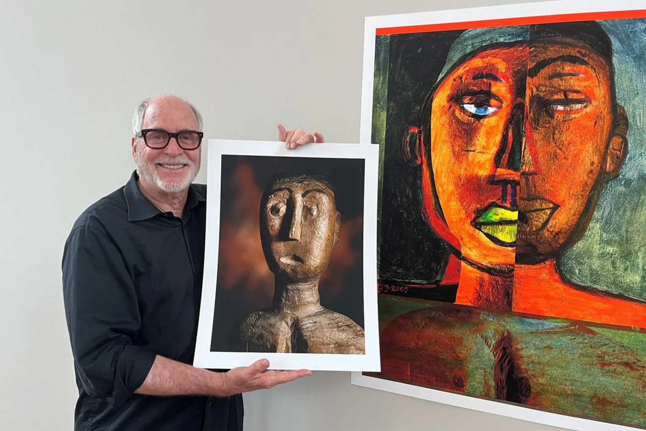 Ein älterer Mann mit schwarzer Brille hält ein Foto einer Skulptur.