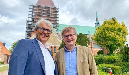 Zwei Männer stehen lächelnd vor einer Kirche