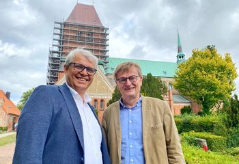Zwei Männer stehen lächelnd vor einer Kirche - Copyright: Bastian Modrow