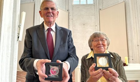 Zwei Personen halten eine Medaille in die Kamera