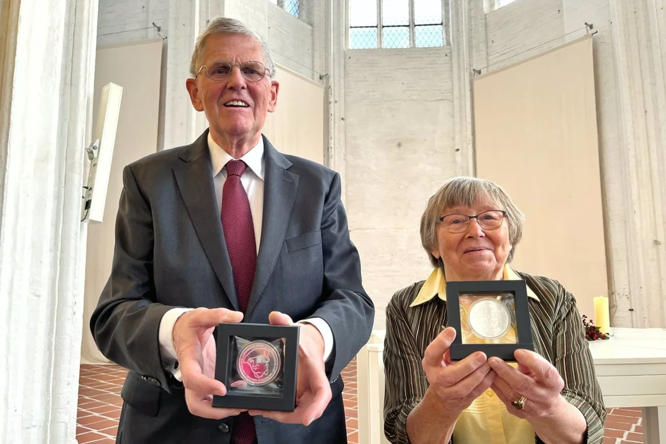 Zwei Personen halten eine Medaille in die Kamera