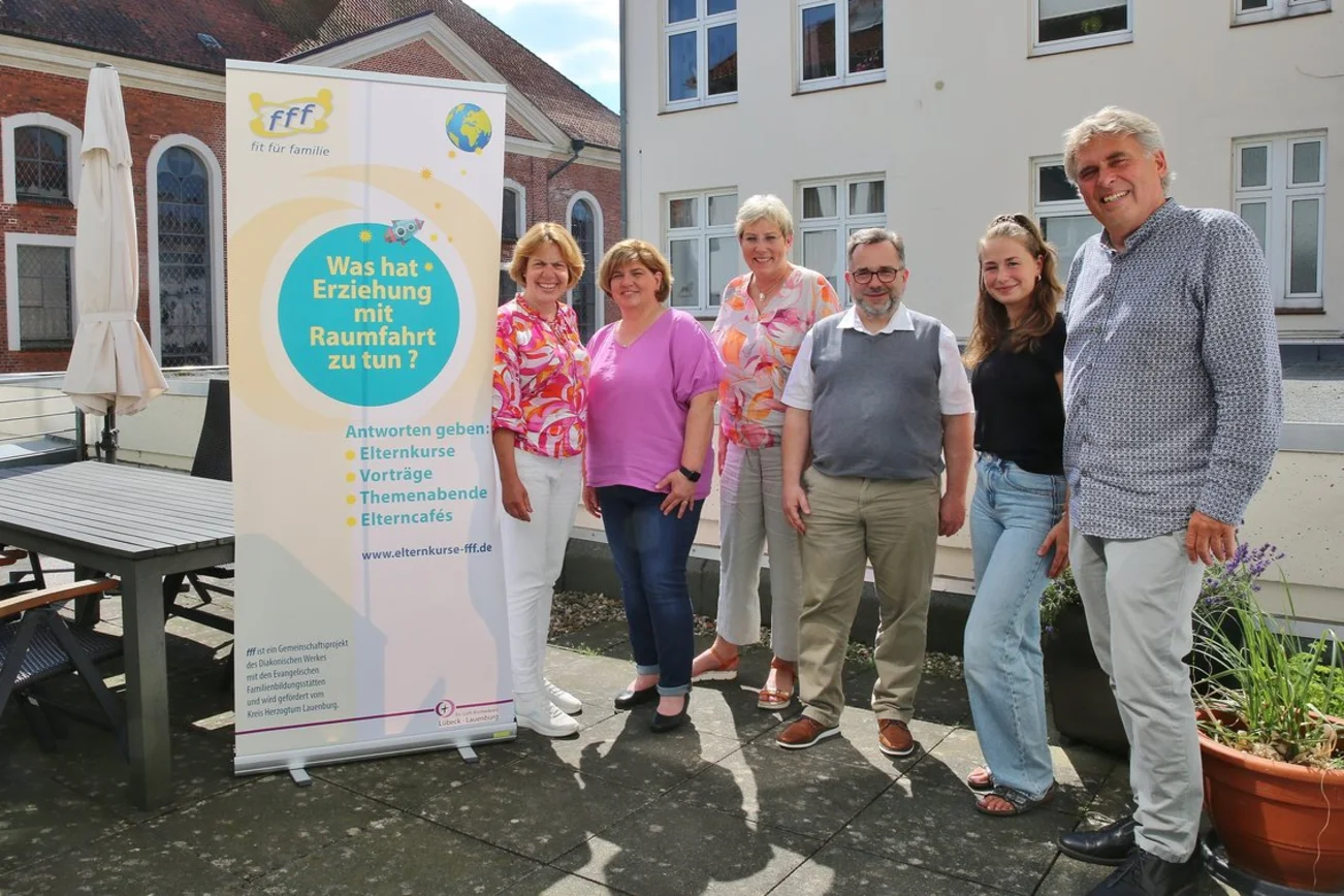 Mehrere Frauen und Männer stehen draußen neben einem hochformatigen Banner.
