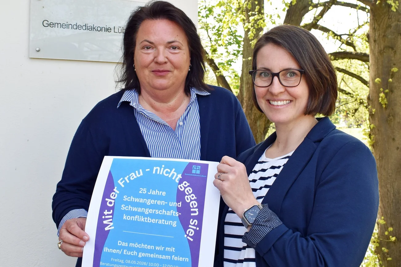 Zwei Frauen halten ein Plakat in die Kamera.