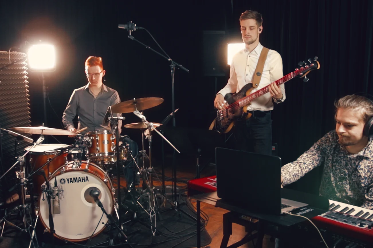 Blick in einen Probenraum, in dem drei Musiker an ihren Instrumenten zu sehen sind. 