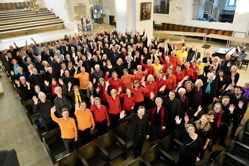 Ein großer Chor in einer Kirche von oben fotografiert winkt in die Kamera.