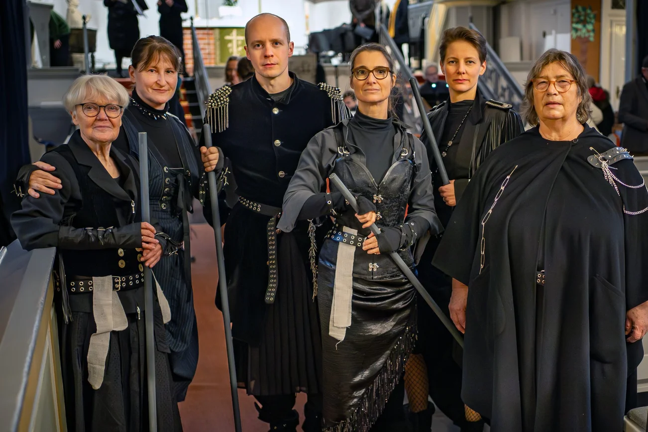 Mehrere Personen in schwarzer kriegerischer Verkleidung stehen als Gruppe zusammen und schauen in die Kamera.