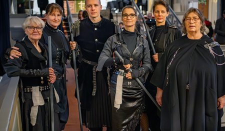 Mehrere Personen in schwarzer kriegerischer Verkleidung stehen als Gruppe zusammen und schauen in die Kamera.