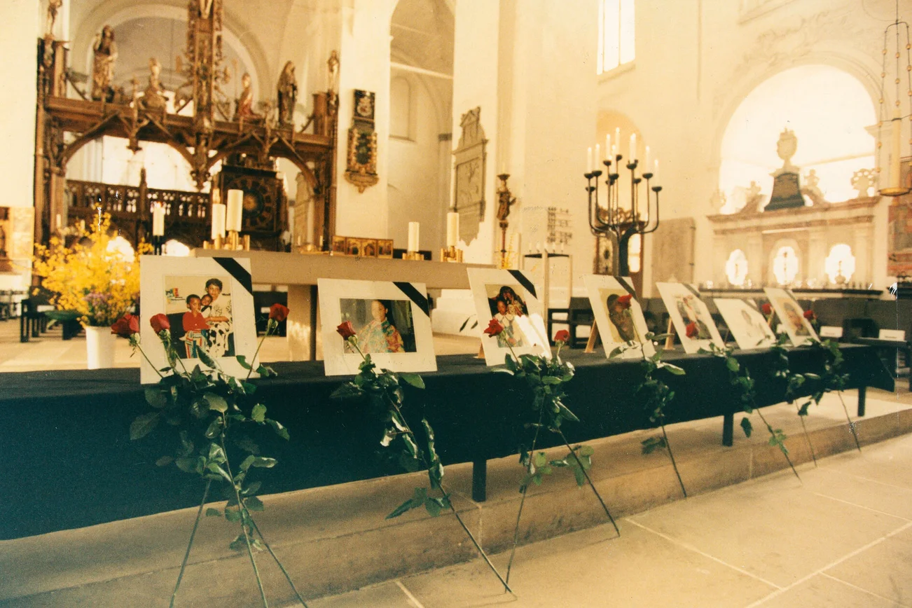 Blick in eine Kirche, in der Bilderrahmen mit Fotos und mit einer Rose aufgestellt sind