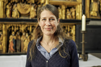 Pastorin Inga Meißner steht vor dem Altar. Auf dem Tisch hinter hier steht rechts eine Kerze. Frau Meißner hat lange braune Haare. Sie schaut in die Kamera. - Copyright: Thorsten Wulff