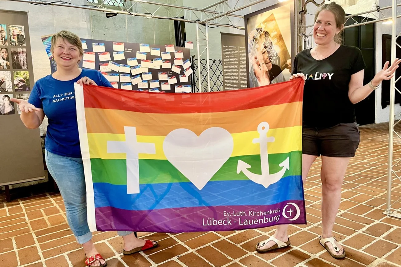 Zwei menschen mit einer bunten Flagge stehen lächelnd in einer Kirche. 