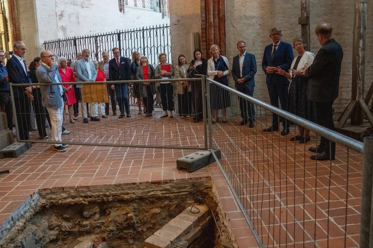 Menschen stehen an einer Grabungsstelle in einer Kirche