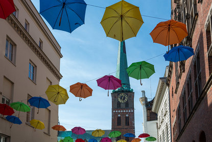 Aufgespannte Regenschirme in verschiedenen Farben, an mehreren Seilen aufgehängt - Im Hintergrund St. Jakobi Lübeck - Copyright: Monika Glende