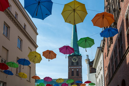 Aufgespannte Regenschirme in verschiedenen Farben, an mehreren Seilen aufgehängt - Im Hintergrund St. Jakobi Lübeck - Copyright: Monika Glende