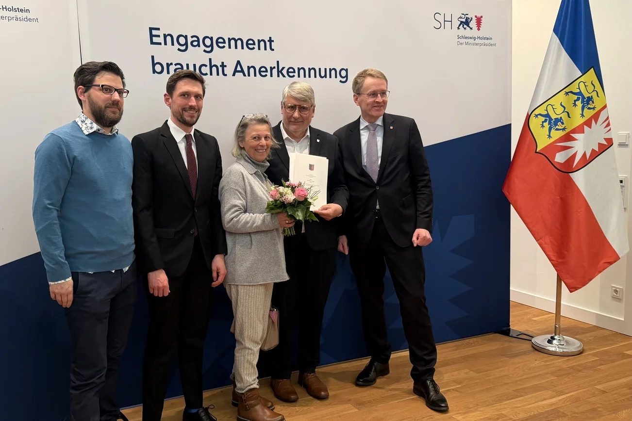 Eine Gruppe Menschen steht neben einer Schleswig-Holstein-Fahne.