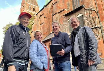 Drei Männer und eine Frau stehen vor einer Kirche und lächeln in die Kamera. - Copyright: Bastian Modrow