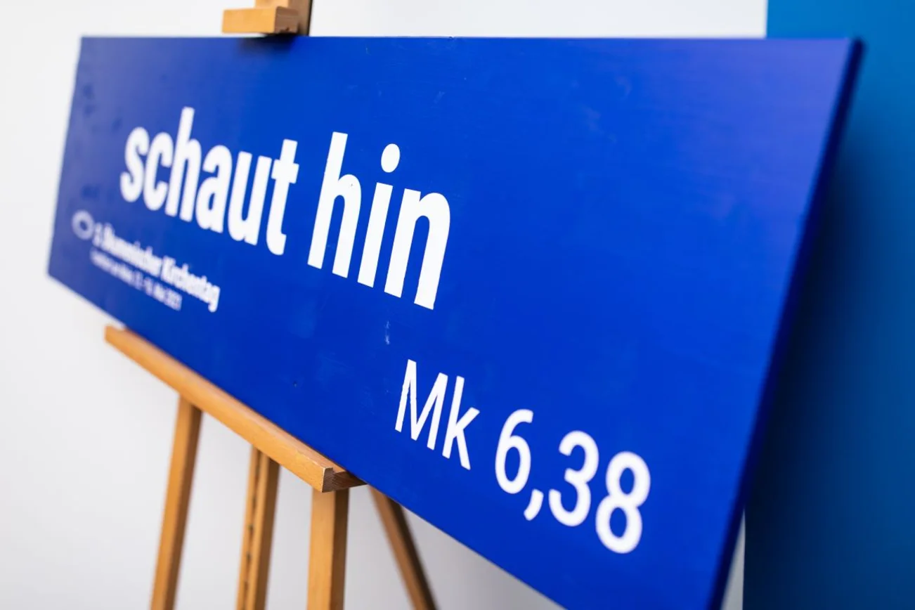 Ein blaues Schild auf einer Staffelei mit der weißen Aufschrift Schaut hin.