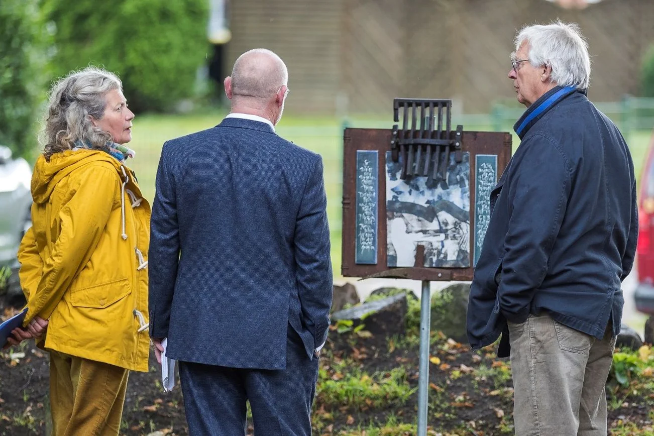 Zwei Künstler im Dialog mit einem Besucher vor einer Skulptur.