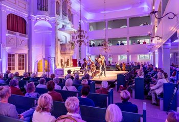 Ein Kirchraum. Vor dem Altar eine Bühne. Menschen sitzen in Reihen rund um die Bühne. Auf der Bühne Ballett. - Copyright: Dirk Eisermann