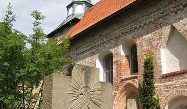 Friedhof St. Georgsberg - Copyright: contactImageCopyright_stringS Ein Steinkreuz mit einer Abbildung der Sonne, davor eine Sichel mit einem Büschel Getreide. - Copyright: contactImageCopyright_stringS