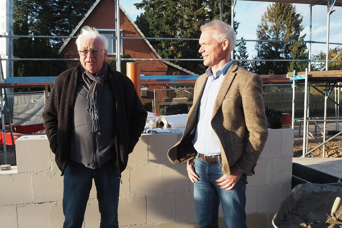 Zwei Männer stehen lachend auf einer Baustelle.