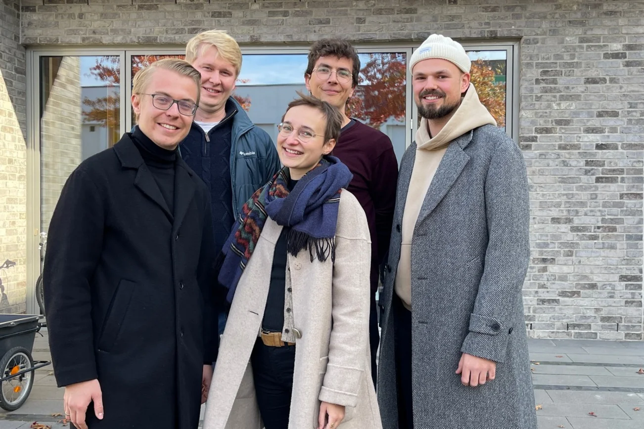 vier Männer und eine Frau stehen warm angezogen vor einem Backsteingebäude