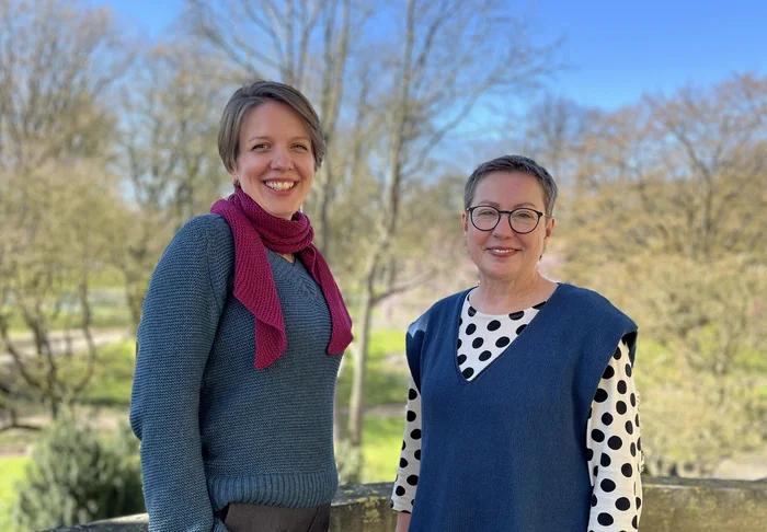 Zwei Frauen stehen im Freien und lächeln in die Kamera.