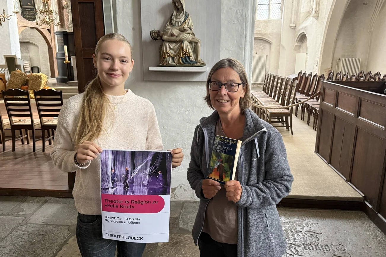 Zwei Frauen stehen mit einem Plakat in einer Kirche.